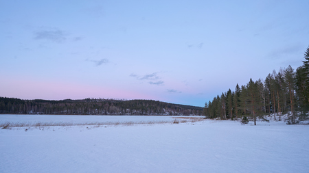 Snowy landscape with frozen lake, field and forestの写真素材