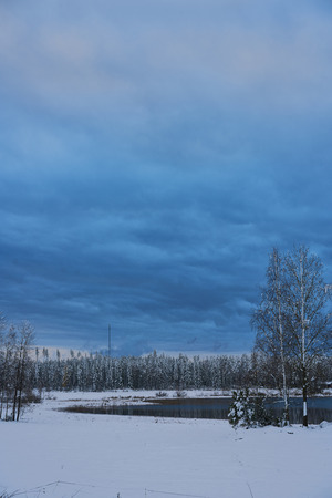 Dark clouds over lake and field in winterの写真素材