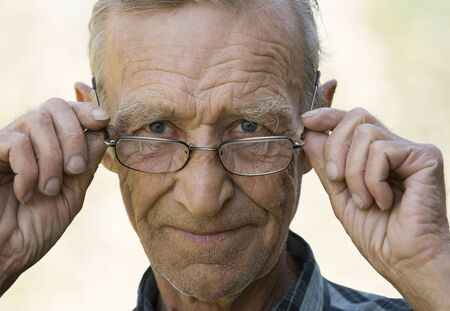 Smiling elderly the man, holding with hands glasses