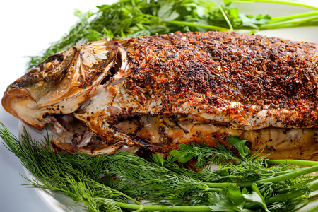Carp baked with spices on a platter with fresh dill and parsley