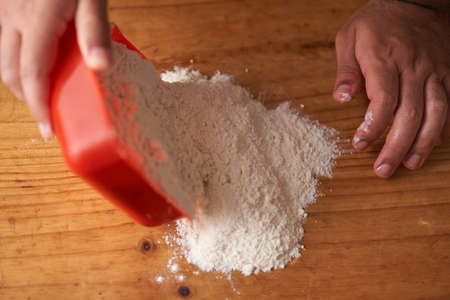 man empties portion of flour on wooden table