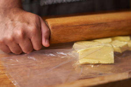 Man with rolling pin stretches butter for preparation with fat. smelly kitchen