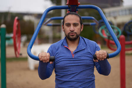 man in blue t-shirt performs body weight exercises in public park. Sports session