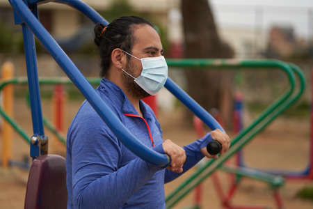 man in blue t-shirt with chinstrap performs body weight exercises in public park. side shot. Sports...