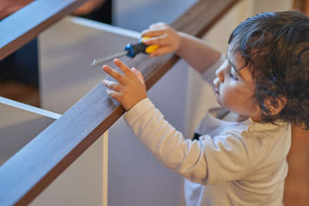 They are plays with screwdriver while his father assembles wooden furniture at home. Carpentry and...