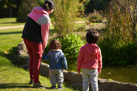 Mother with two children on their backs walking in a park. Woman with two children in a garden....