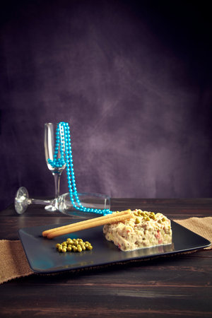 Vertical capture of a Russian Salad in a dark mood with two champagne glasses behindの写真素材