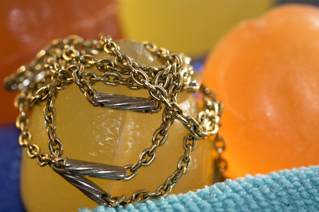gold necklace and bracelet approached at some colored bath soaps for a concept of wellness and...