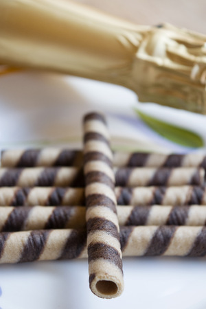 rolled wafers at the chocolate on a white dish and champagne bottleの写真素材