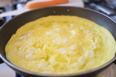 beaten eggs in pan with parmesan pieces to make an omeletteの写真素材