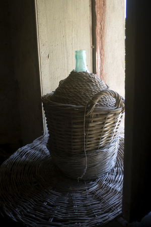 demijohn covered with wicker and straw illumined between a windowの写真素材