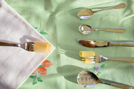 geometric composition with top view between raw pasta and silver cutlery
