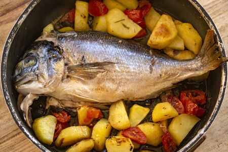 baked sea bream with potatoes and tomatoes in a baking pan