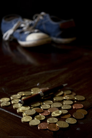 coins and wooden pen on a small table with a pair of shoes in the backgroundの写真素材