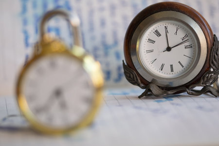 small table clock with a pocket watch out of focus in the foreground