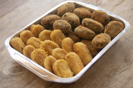 fried potatoes croquettes and eggplant meatballs arranged in an aluminum pan