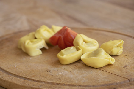 wooden cutting board with meat tortellini and fresh tomatoの写真素材