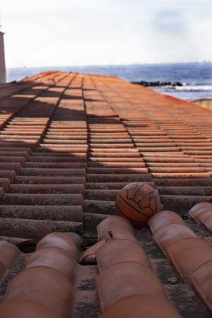 series of roofing-tile with an old ball with the sea and the horizon in the backgroundの写真素材