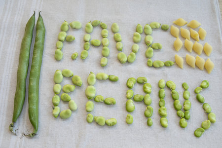 intence green broad beans, both in their pods and shelled, are arranged alongside dry conchiglie...