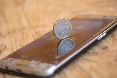 Euro coin remaining on a cracked smartphone screen, symbolizing economic value versus fragile or obsolete technology. Digital decay conceivedの写真素材