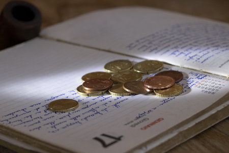 an open, handwritten diary with euro cent coins scattered on its pages, symbolizing personal finance, budgeting, and daily planningの写真素材