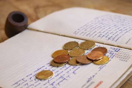 A scattering of euro coins lies on the pages of an aged, handwritten journal, suggesting personal finances or past expensesの写真素材