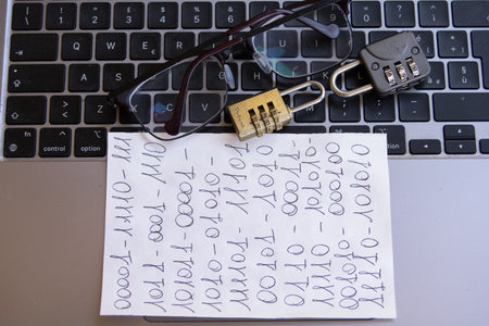 a close-up of a laptop keyboard with a combination padlock, a small brass lock, and glassesの写真素材