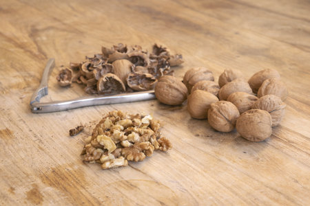fresh walnuts whole and cracked open showing shells and kernels with nutcracker on wood surface