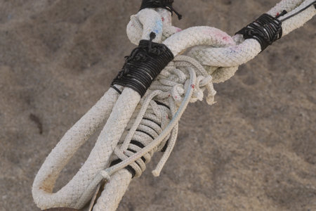 close-up detail of heavy white nautical ropes secured with tight black lashing and complex knotwork on a blurred sandy background. strength, connection, and craftsmanship conceptの写真素材
