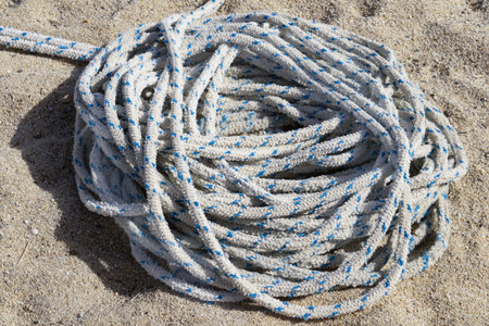 close-up of thick white and blue spotted nautical rope lying coiled on warm, textured yellow sand....