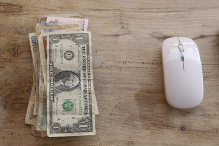 concept of digital economy fintech and online payment a stack of currency notes including a us dollar bill next to two computer mice on a wooden surfaceの写真素材