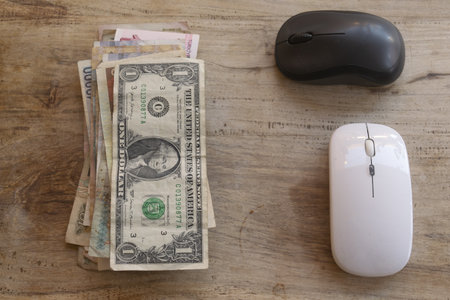 concept of digital economy fintech and online payment a stack of currency notes including a us dollar bill next to two computer mice on a wooden surfaceの写真素材