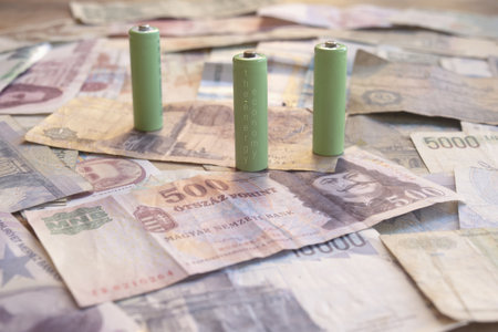 three green rechargeable batteries labeled the energy economy on several international currency banknotes symbolizing sustainable power financial system and green economic transitionの写真素材