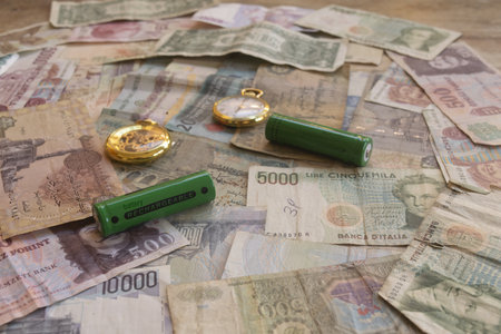 green rechargeable batteries placed on collection of old international paper money including italian lire and hungarian forint with antique pocket watchの写真素材