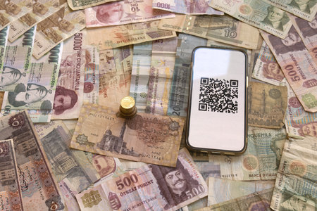 stack of coins next to smartphone displaying qr code on bed of various international banknotes...