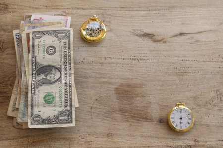 conceptual still life showing time is money theme with assorted currency bills and golden pocket watches arranged on rustic wooden surfaceの写真素材
