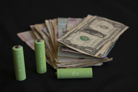 green batteries labeled ev with cash money symbolizing electric vehicle costs charging expenses and sustainable transport investment conceptの写真素材