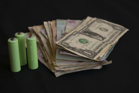 Green batteries with the word price written on them next to banknotes representing energy prices, electricity market costs and consumer spending on energy resourcesの写真素材