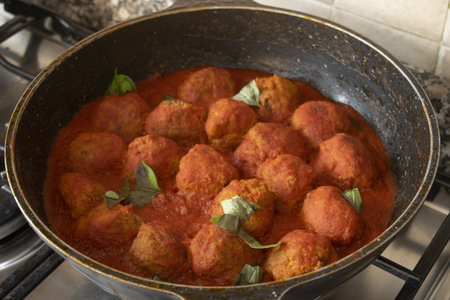 overhead view of homemade meatballs simmered in rich tomato sauce with fresh basil leaves in rustic...