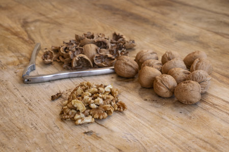 whole and cracked walnuts with shells and nutcracker on rustic wooden table, healthy vegan snack and...