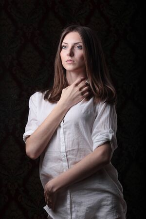 sad girl in a white blouse on a dark backgroundの写真素材