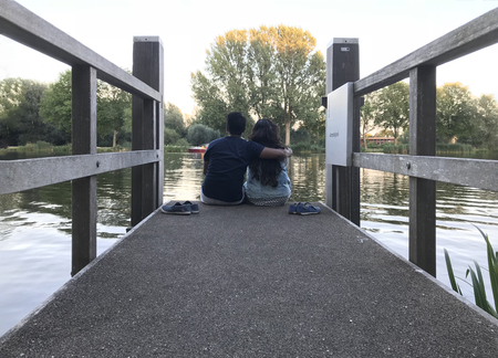 A Couple Sitting on a Small Pier Enjoying the View of River and Trees at Eveningの写真素材