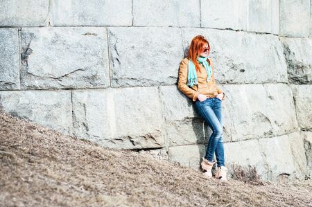 Nice red-haired girl in sunglasses lean on stone wall.の写真素材