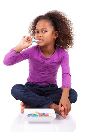 Little African Asian girl eating candy, isolated on white backgroundの写真素材