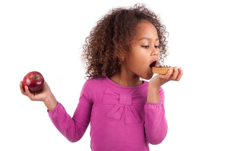 Little African Asian girl eating a chocolate cake and holding an apple, isolated on white backgroundの写真素材