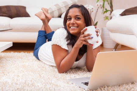 Young happy indian lying down on the floor woman using a laptopの写真素材