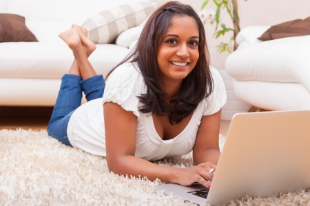 Young happy indian lying down on the floor woman using a laptopの写真素材