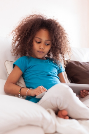 Little african asian girl seated on the couch using a tablet  pcの写真素材