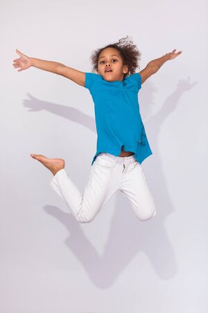 Portrait of cute Young African American girl jumping, over gray backgroundの写真素材