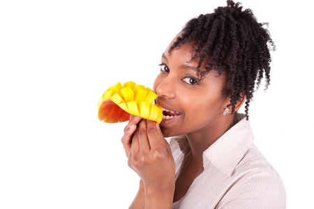 Young happy black / african american woman eating fresh mango isolated on white backgroundの写真素材